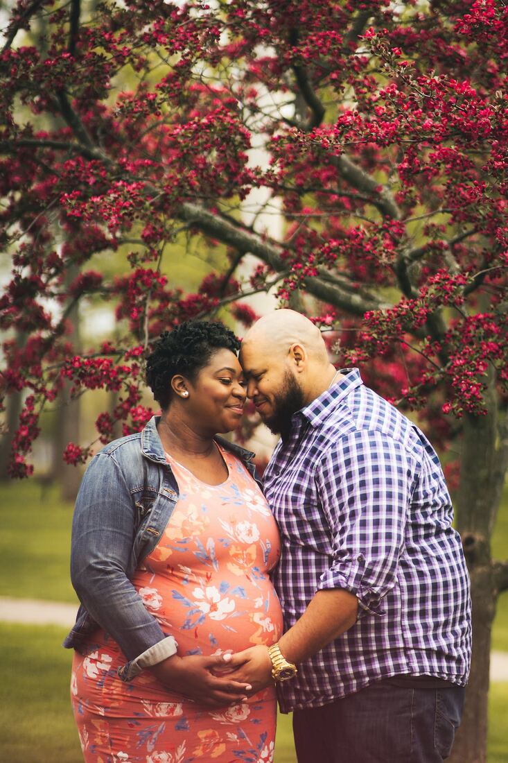 An expectant couple standing forehead to forehead under a blossoming tree