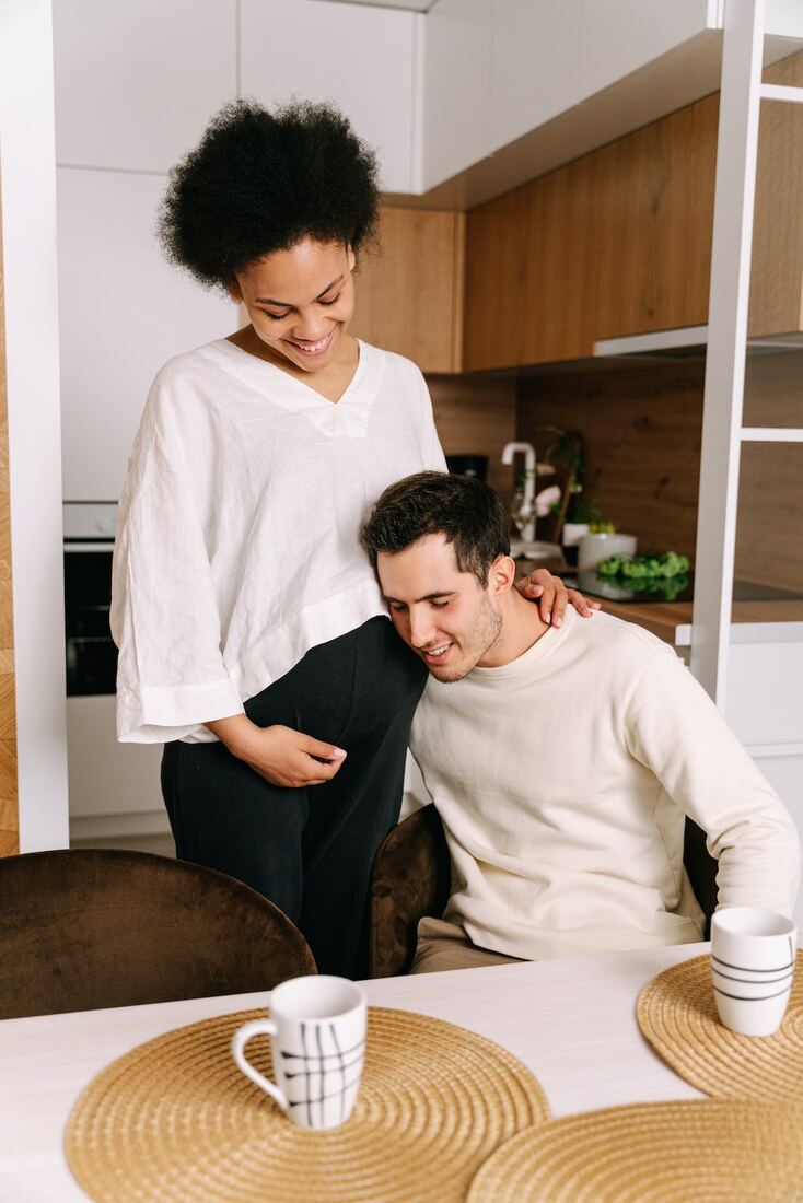 A man resting his head against his pregnant partner in a kitchen