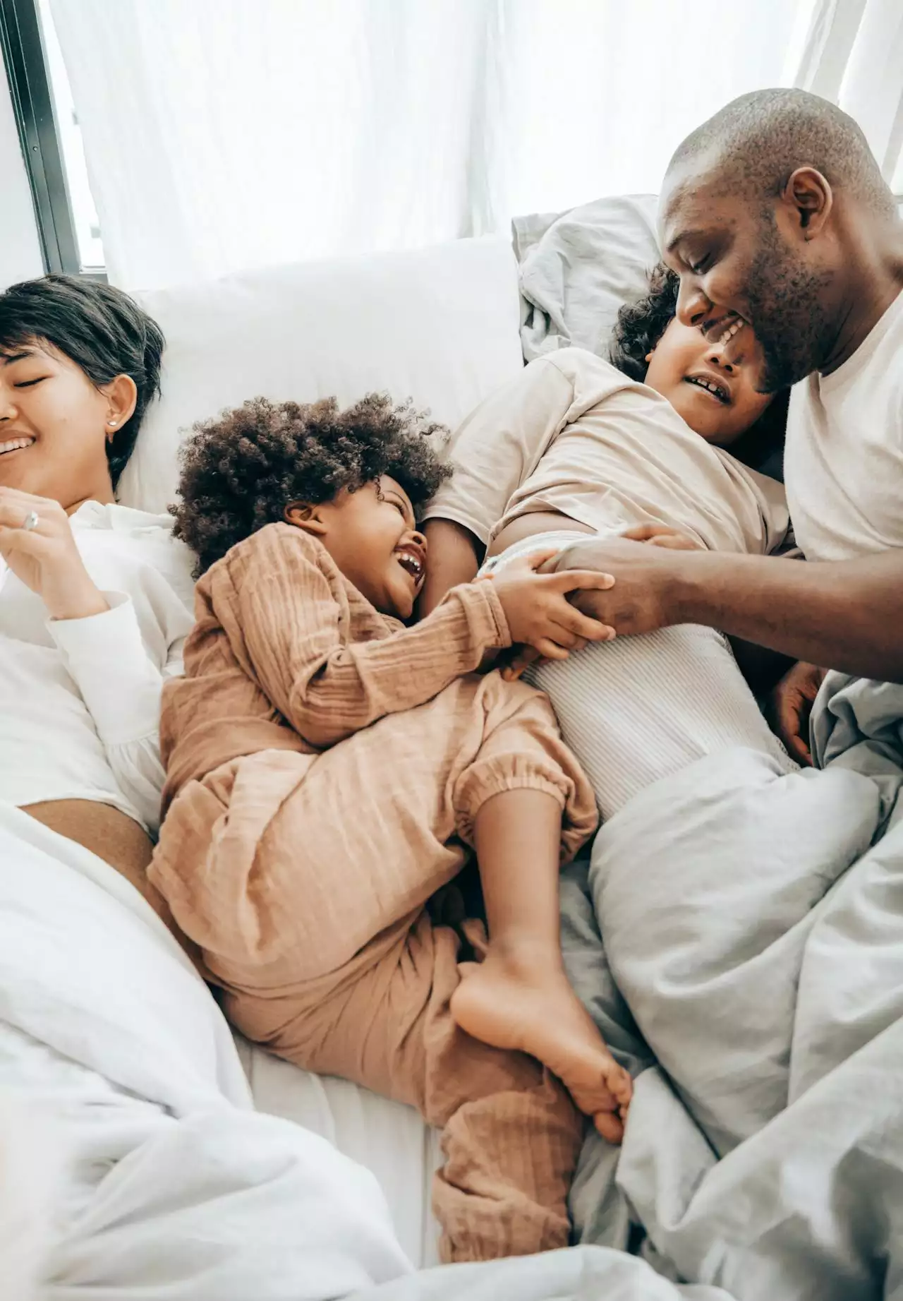 Two parents and two children laughing together on a bed