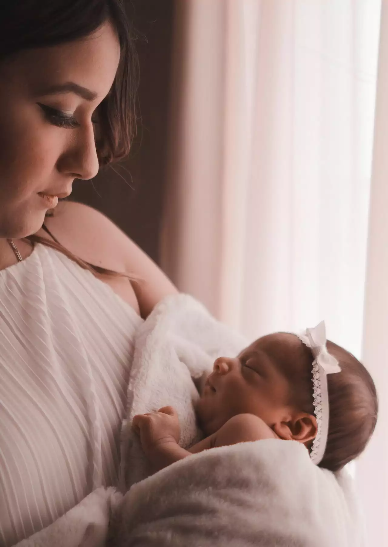 A woman holding a sleeping newborn by a window