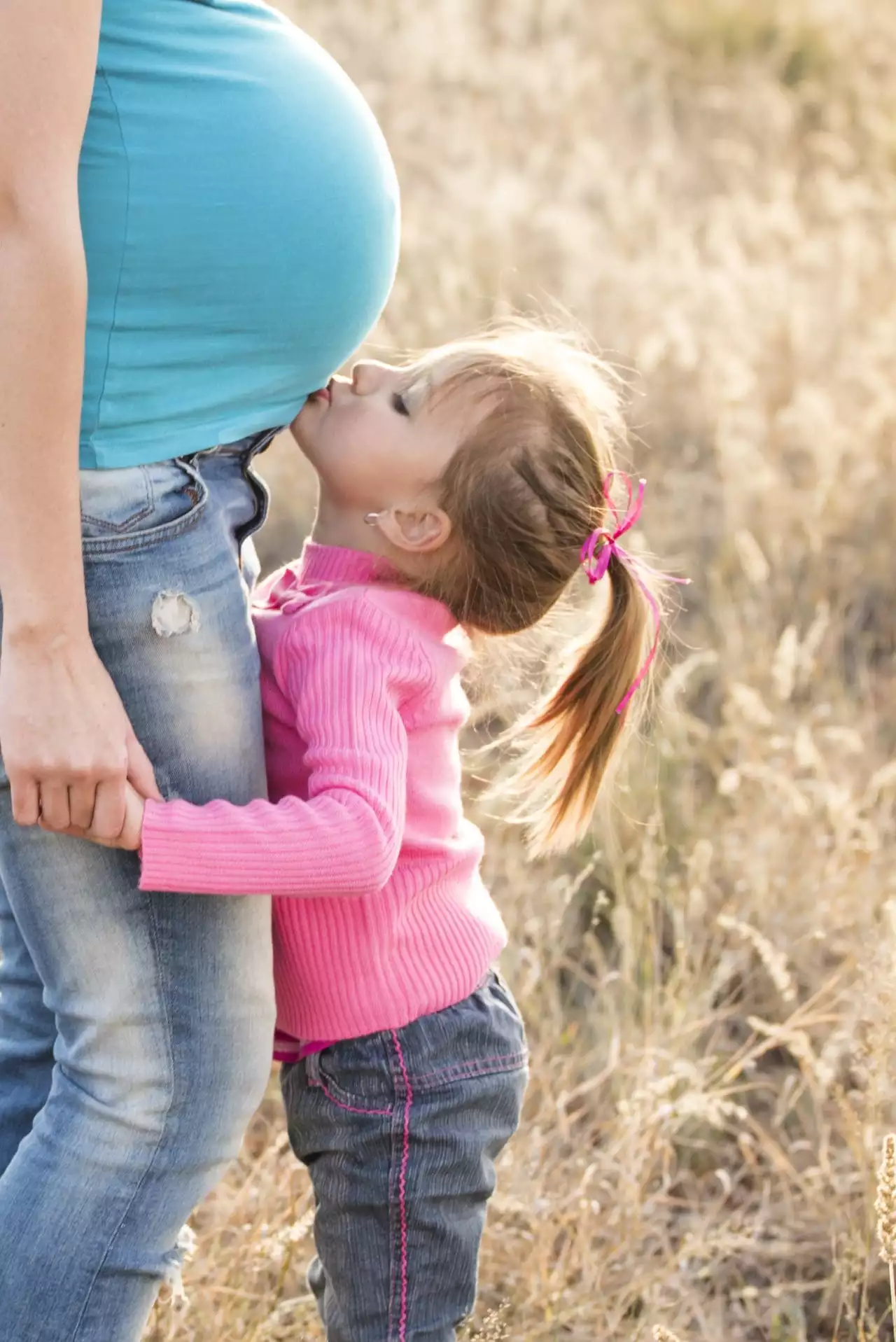 A young girl kissing her mother's pregnant belly in a field